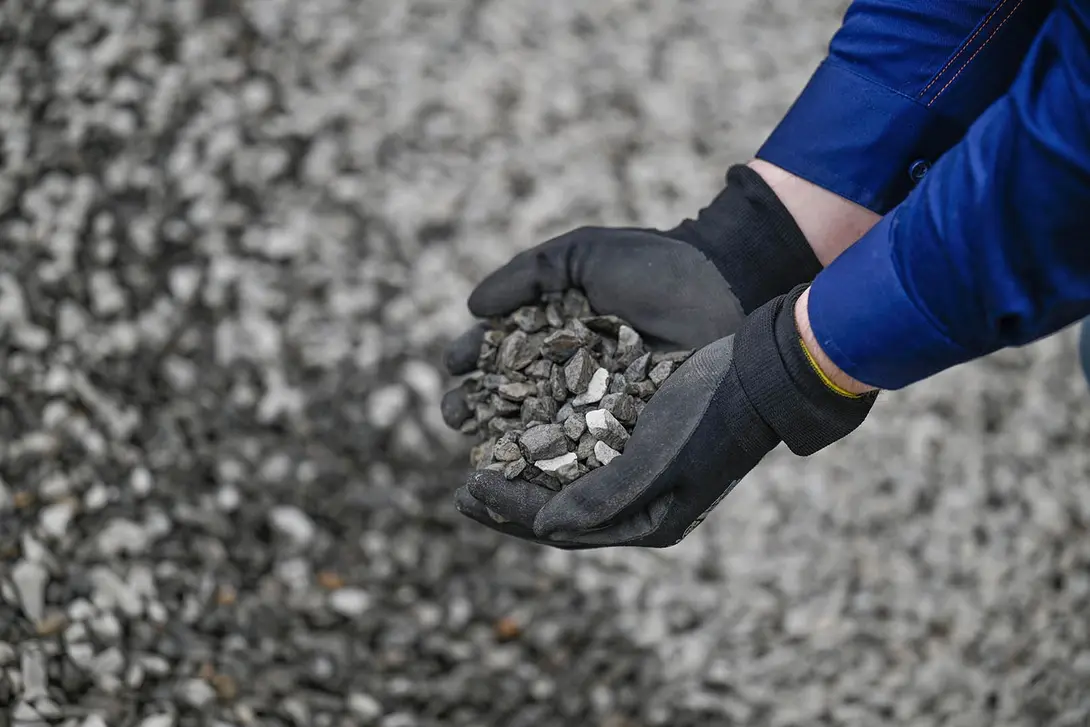 Gloved hands holding recycled aggregate material at a quarry site.