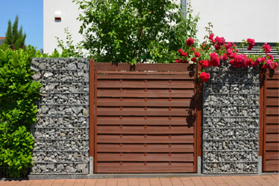 Gabion mattress rock used in a modern fence design, with wire cages filled with stones forming decorative and structural retaining wall elements alongside timber panels.
