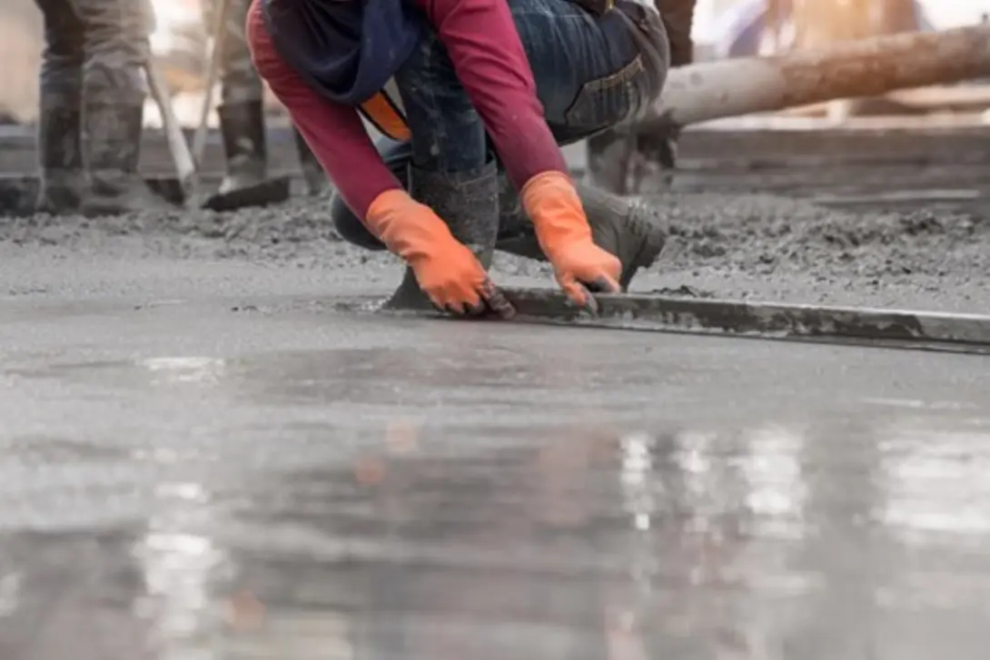 Worker finishing a freshly poured Sureset concrete slab using a hand trowel, creating a smooth surface with fast-setting concrete for efficient construction.
