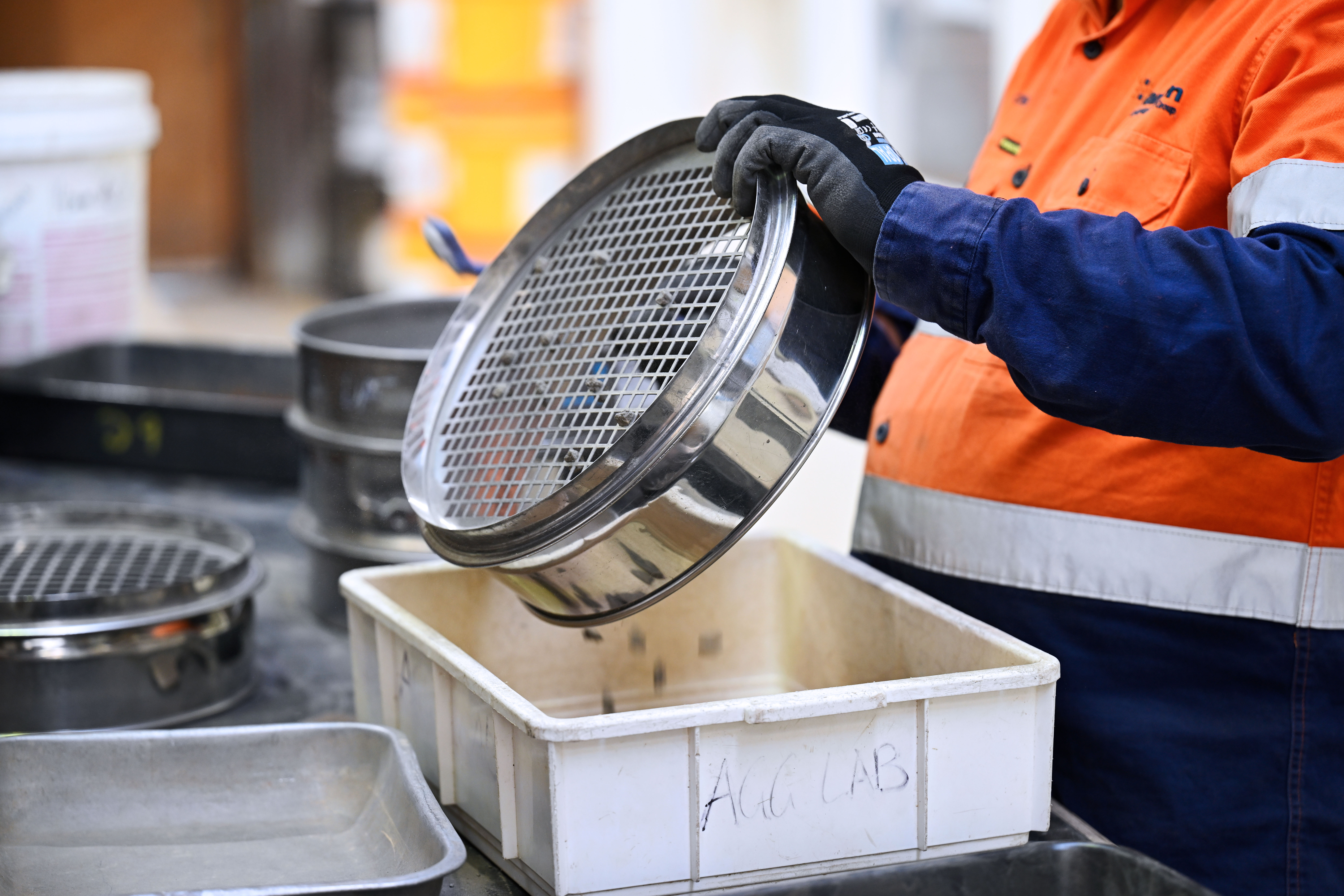 Heidelberg Materials laboratory technician using a test sieve to separate and analyse aggregate samples as part of quality control and technical laboratory testing.