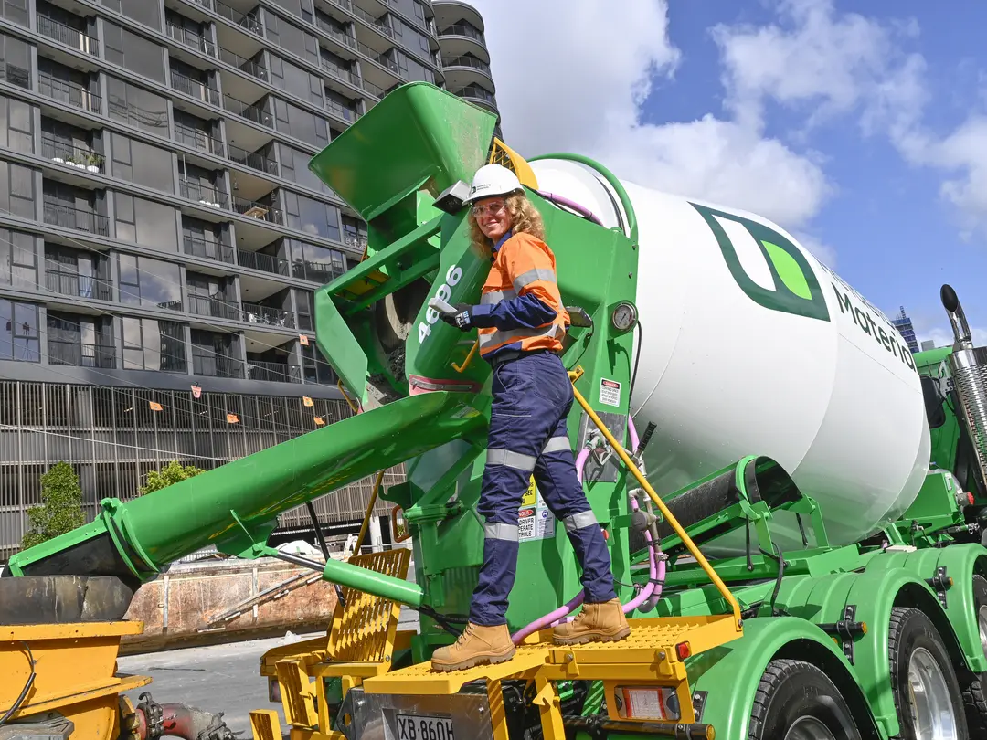 Heidelberg Materials Australia concrete agitator truck delivering concrete at a high-rise construction site, with an employee in PPE standing on the rear platform beside the concrete chute.