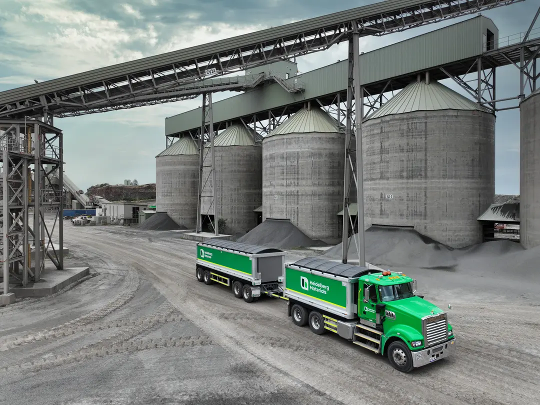Heidelberg Materials Australia haulage truck transporting aggregates at a quarry processing facility with storage silos and material handling infrastructure.