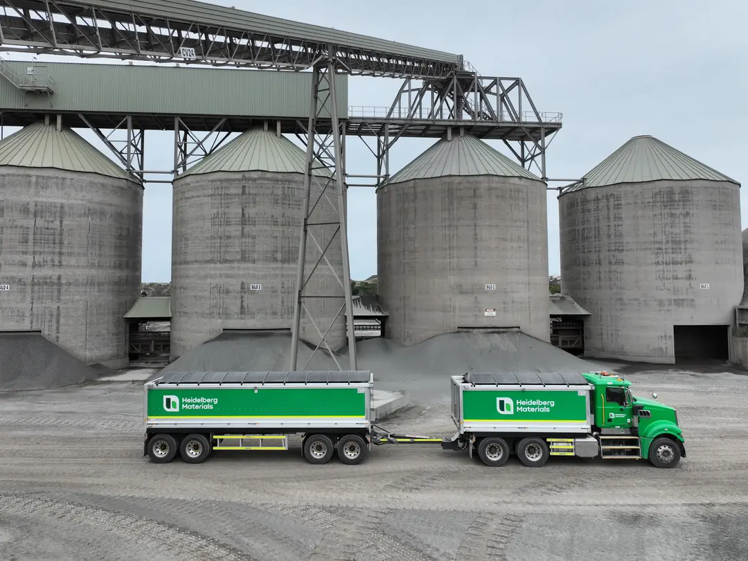 A Heidelberg Materials Australia bulk haulage truck parked in front of large concrete storage silos at a quarry and construction materials production site.